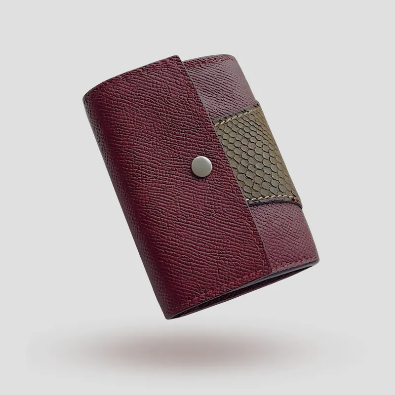 A custom wallet handcrafted in burgundy premium cowhide leather, featuring a bold, asymmetrical wrap accent in salmon leather, paired with a supple goatskin lining.